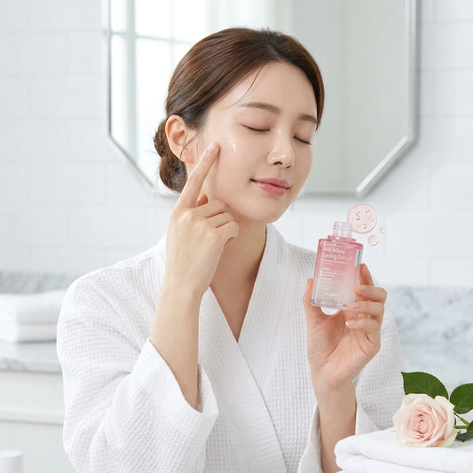 Woman applying to face of Dr. esthé Anti-Mela Toning Serum with a white cap and a pink-to-clear gradient liquid.