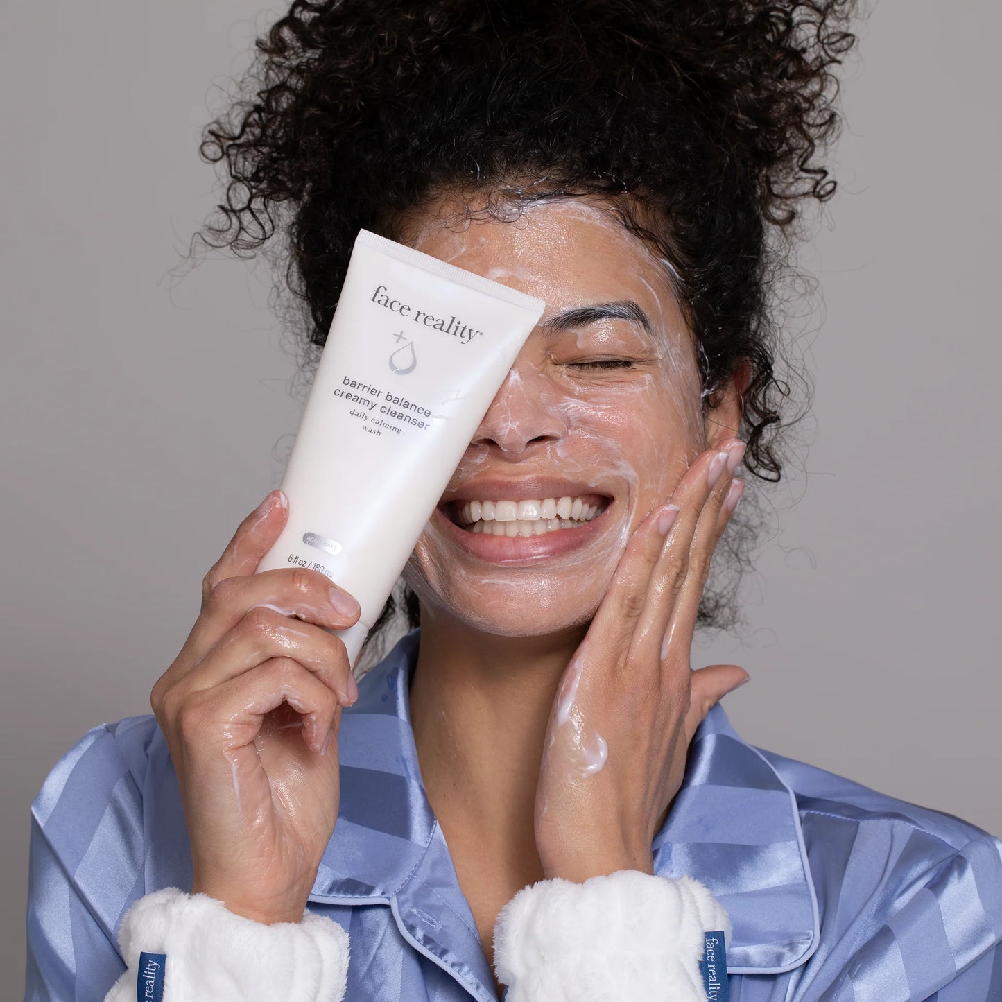 Woman washing her face with a 'face reality' barrier balance creamy cleanser wearing a robe.