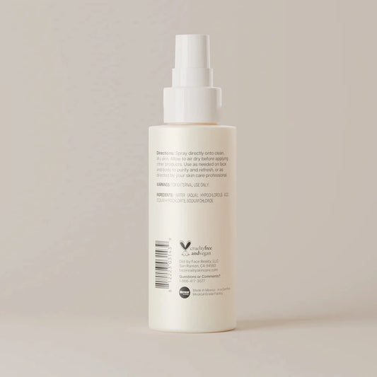 A tall, off-white pump bottle with a white spray nozzle, showing the back side with printed text and a barcode, set against a solid, warm beige background.