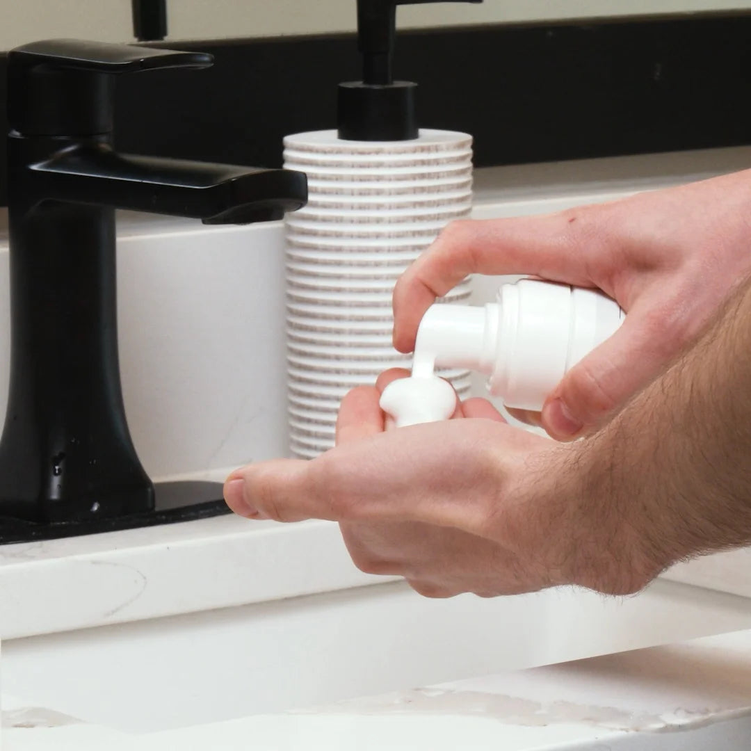 Hand using a Glymed Plus Foaming Cleanser dispenser in a sink