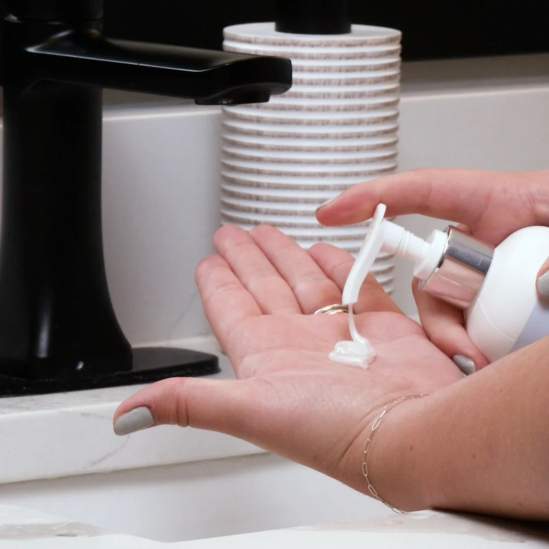 Hand using a Glymed Plus Glycolic Facial Cleanser with 10% Glycolic Acid pump bottle with a black faucet