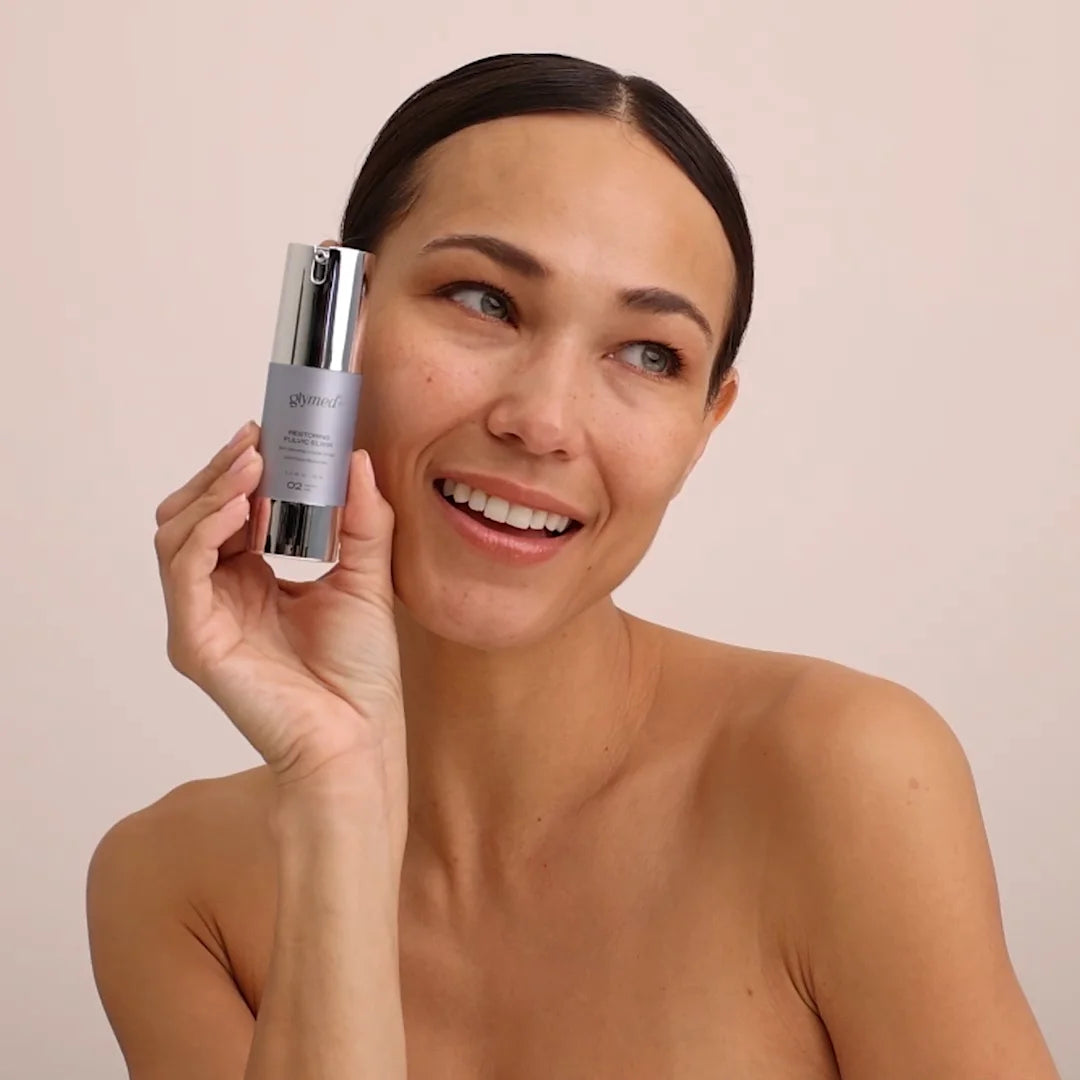 Woman holding Glymed Plus Restoring Fulvic Elixir Serum against a beige background