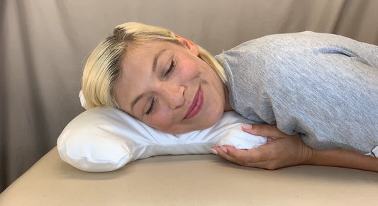 Woman lying on a bed with a white Save My Face Le Grande Adjustable White Satin pillow under her head.