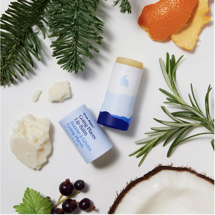 Two lip balm sticks on a white surface with natural elements like leaves and an orange.