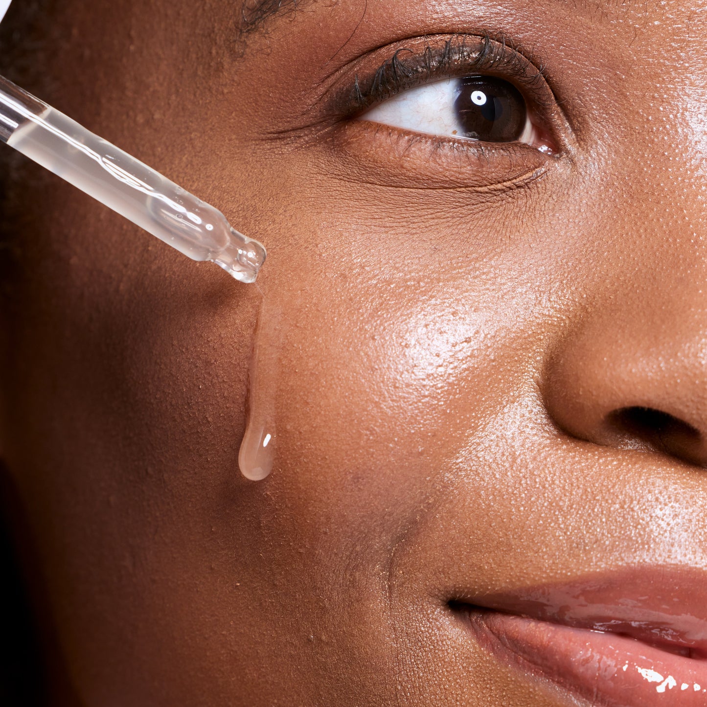 Close-up of a woman applying a dropper of skincare product to her eye.
