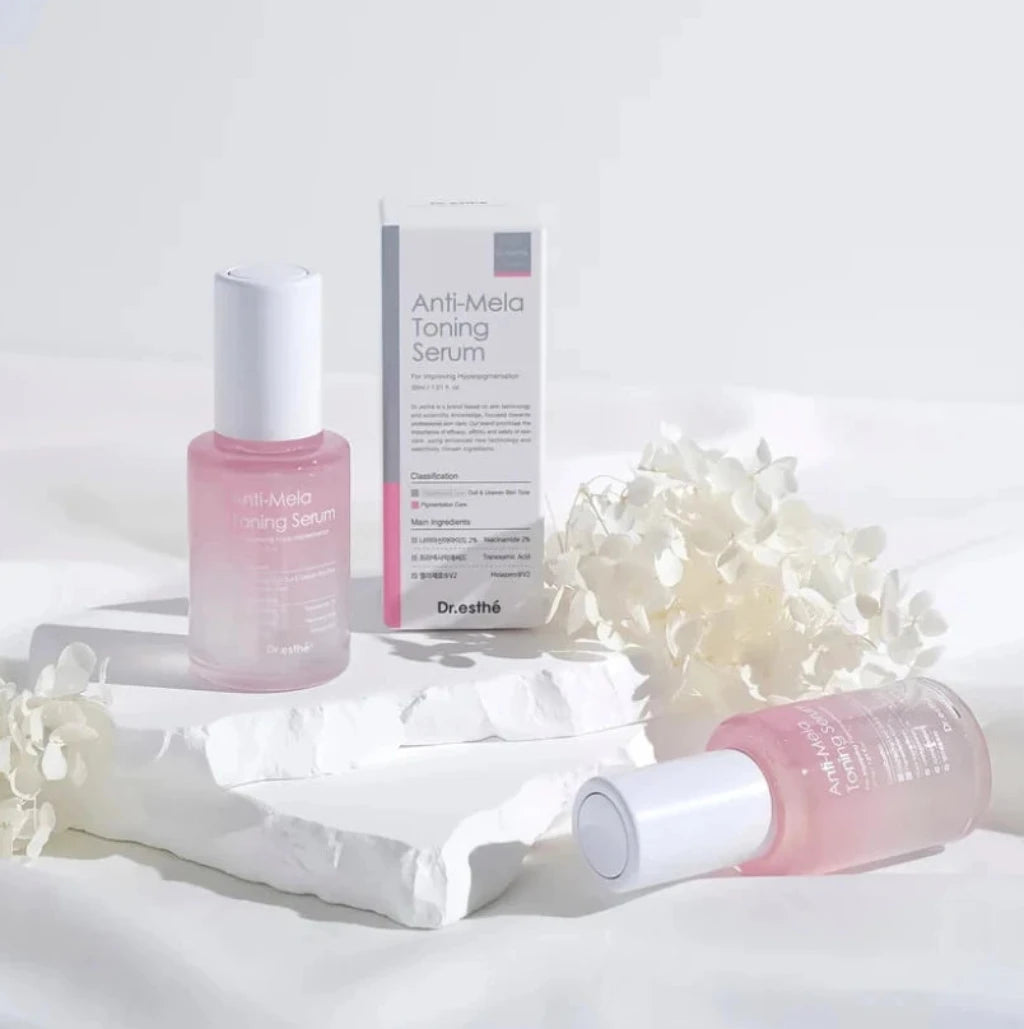 A pink skincare serum bottle and its white product box are displayed on white fabric, accented with small white flowers. The bottle and cap are frosted pink with white, and the box is white with black text.