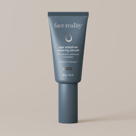 A single cosmetic tube of face reality age adaptive clearing serum, in a muted slate blue-gray color, standing upright against a solid warm beige background.
