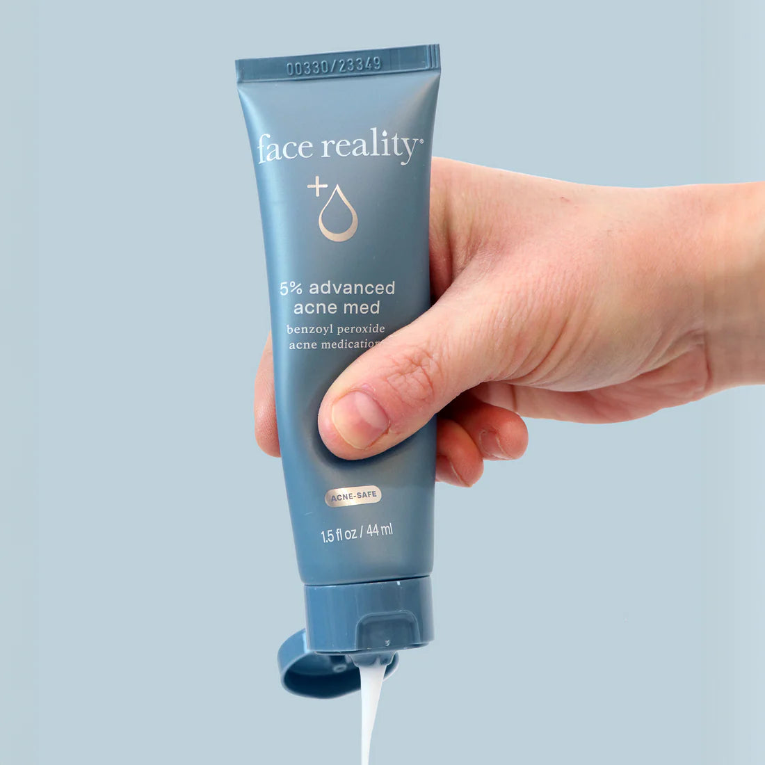 Hand holding a tube of 'face reality' 5% advanced acne med against a light blue background