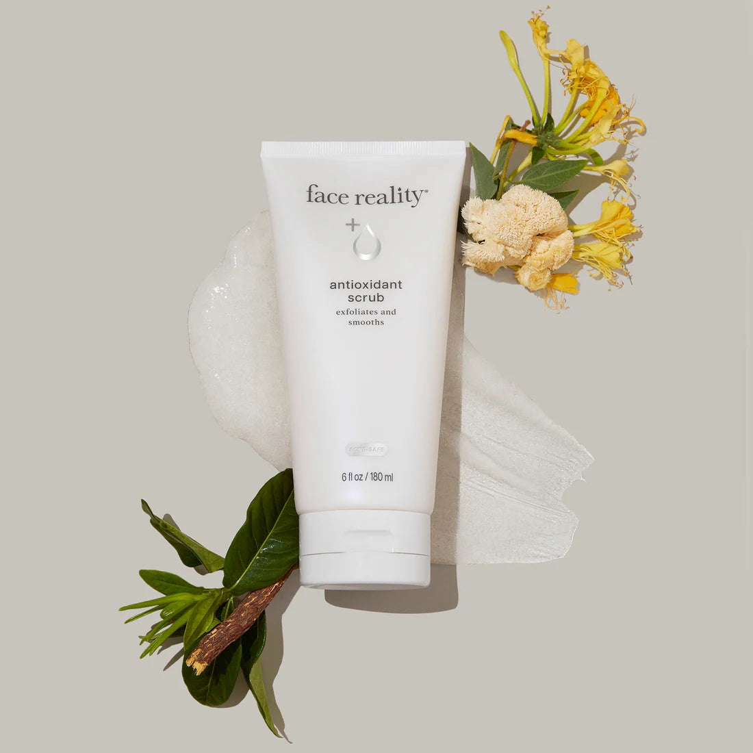 Tube of 'face reality' antioxidant scrub with flowers and leaves on a light background