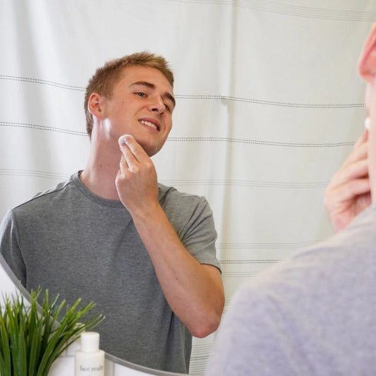 Man applying toner to his neck in front of a mirror
