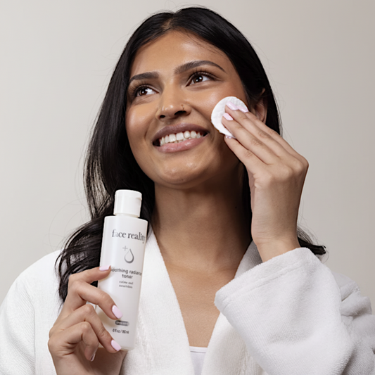Woman applying skincare product with a bottle of Face Reality Soothing Radiance Toner on a beige background
