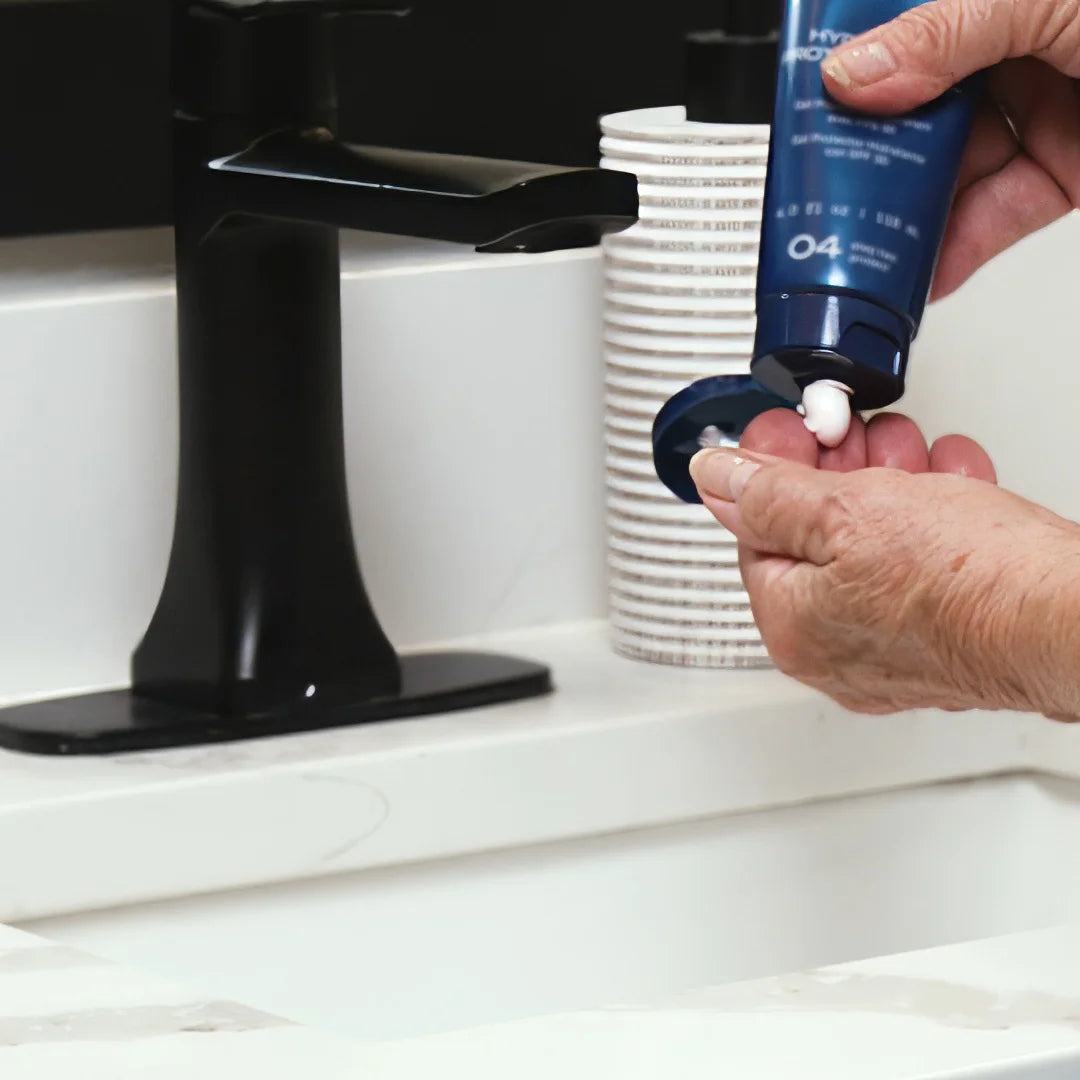 Person applying Glymed Plus Hydrating Protection Gel SPF 30 from a  blue dispenser on a white countertop.
