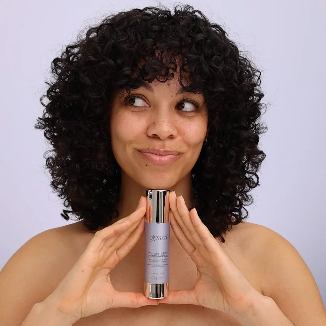 Woman holding bottle of Glymed Plus Oxygen Deep Pore Masque with a plain background