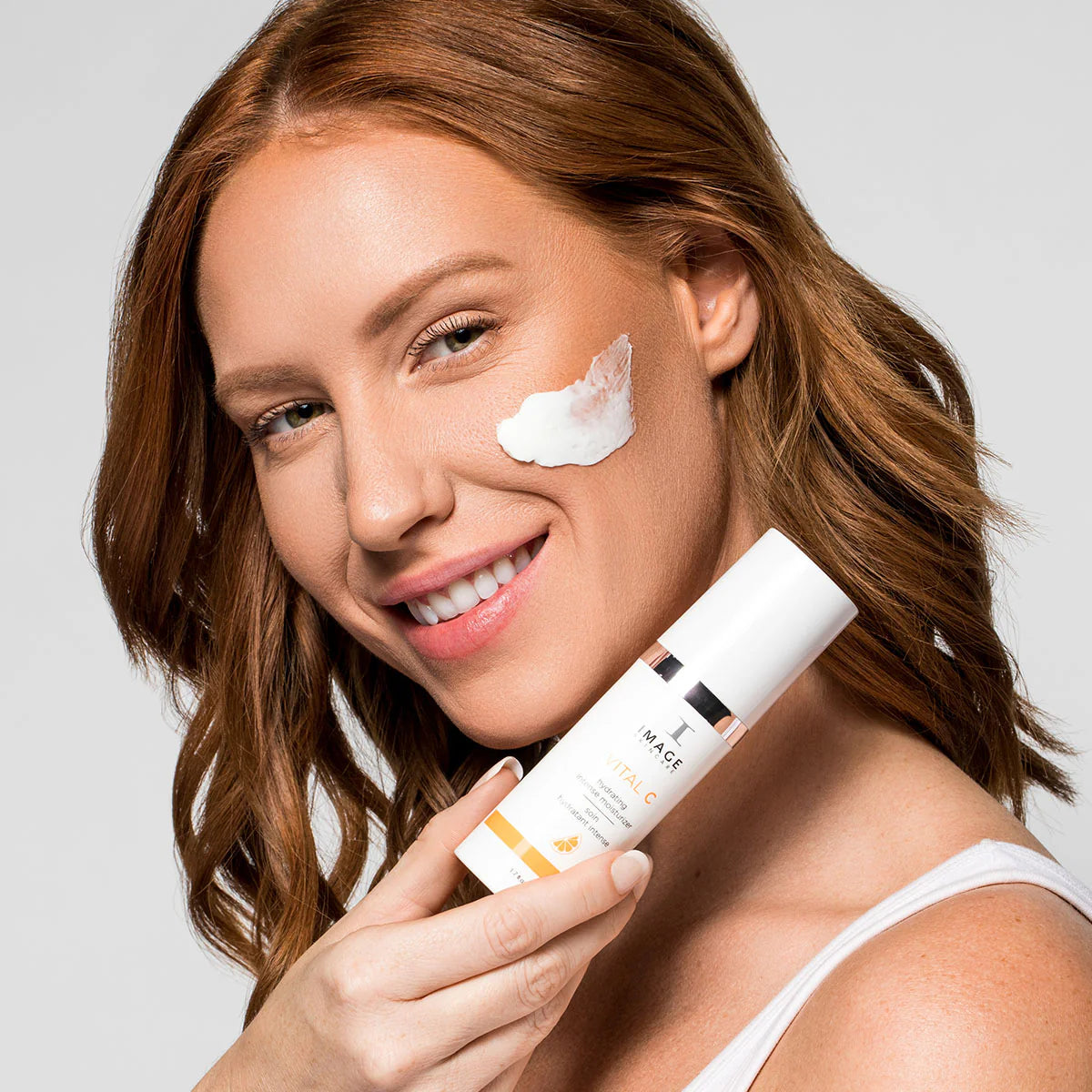 Woman applying sunscreen cream to her face with a bottle of moisturizer.