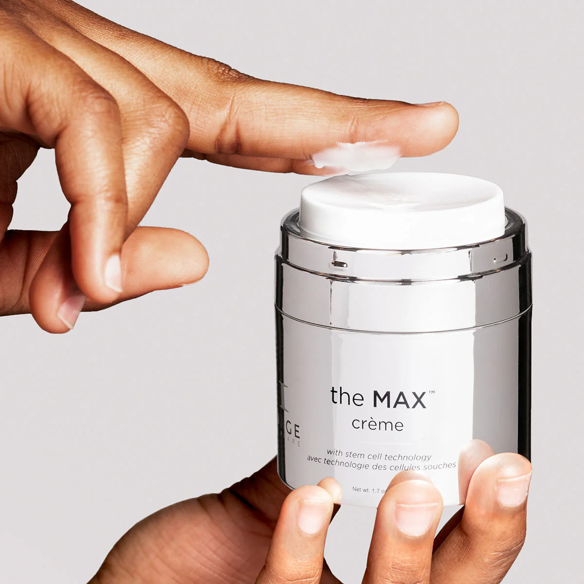 Hand applying cream from a jar labeled 'the MAX crème' on a light gray background