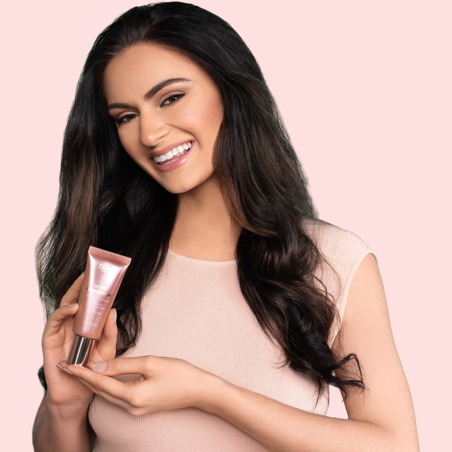 Woman holding Rejuva Minerals Liquid Foundation skincare product against a pink background