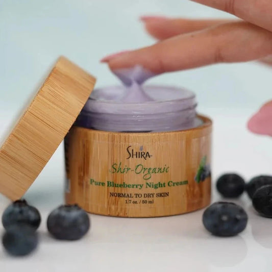 Shira Organic blueberry night cream jar with a hand applying cream and blueberries around it.