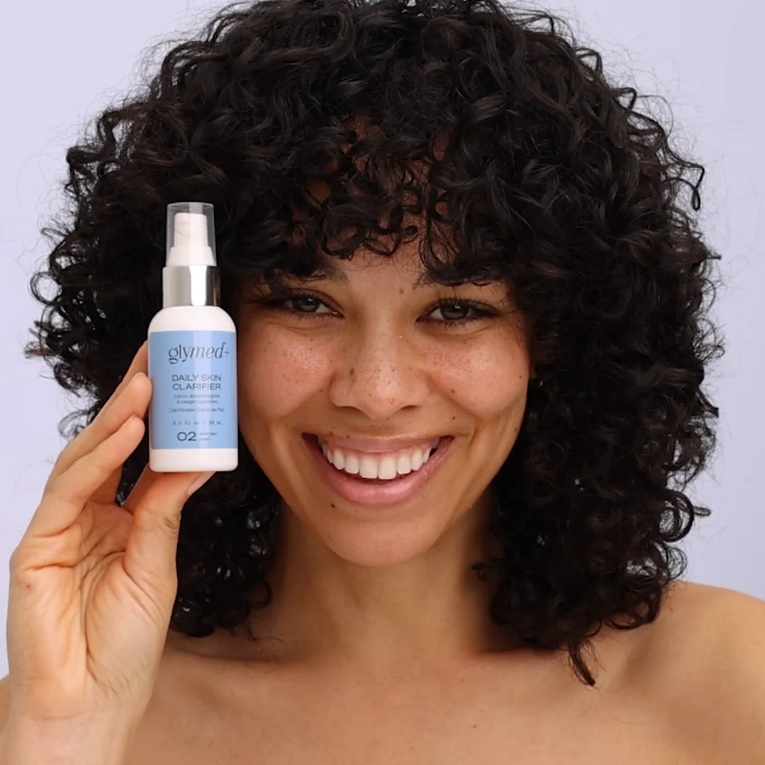 Woman holding a bottle of Glymed product against a plain background