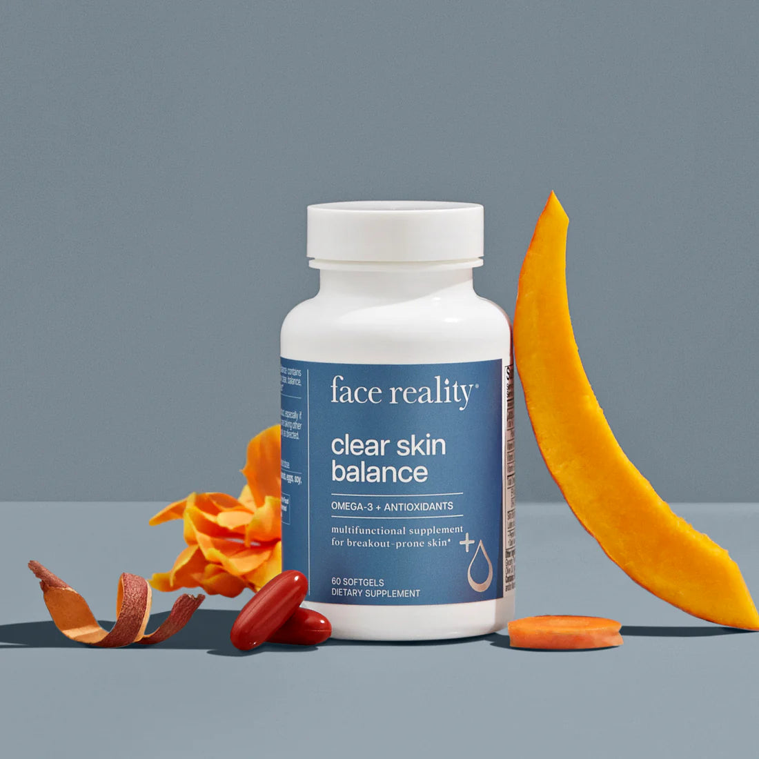 Supplement bottle labeled 'face reality clear skin balance' with orange peel and carrot on a gray background
