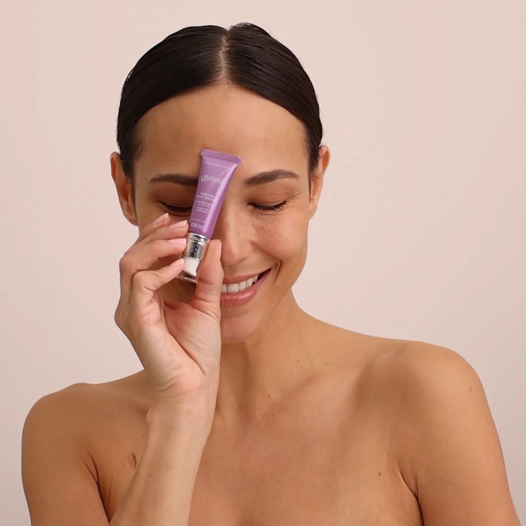 Woman applying eye cream to her face with a beige background