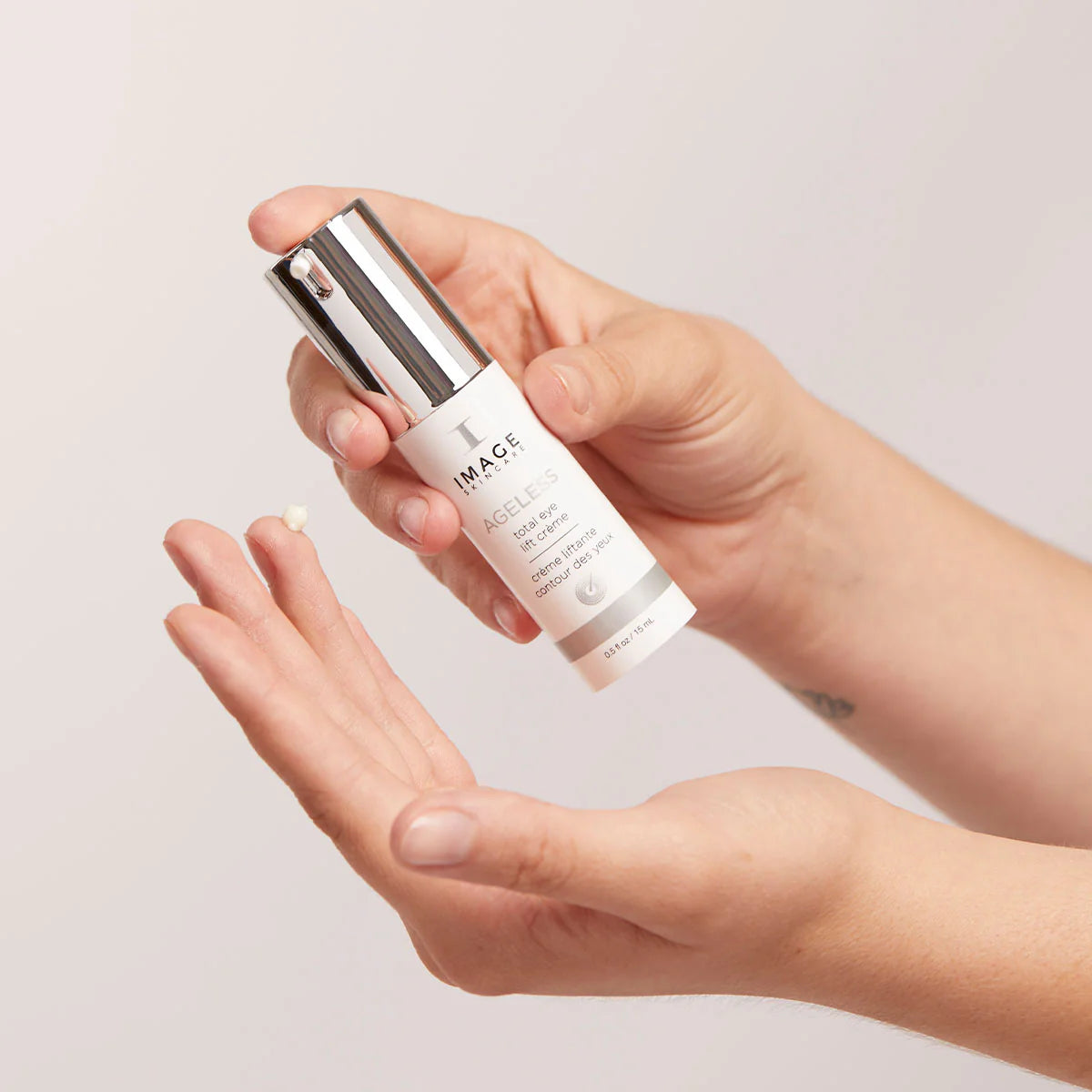 Hand holding a skincare bottle labeled 'IMAGE' Ageless Total Eye Lift Creme against a neutral background