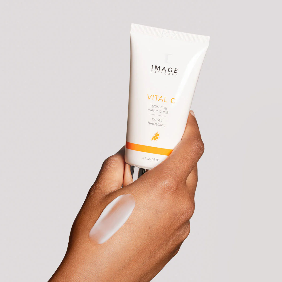 Hand holding a tube of Image Skincare Vital C product on a light gray background