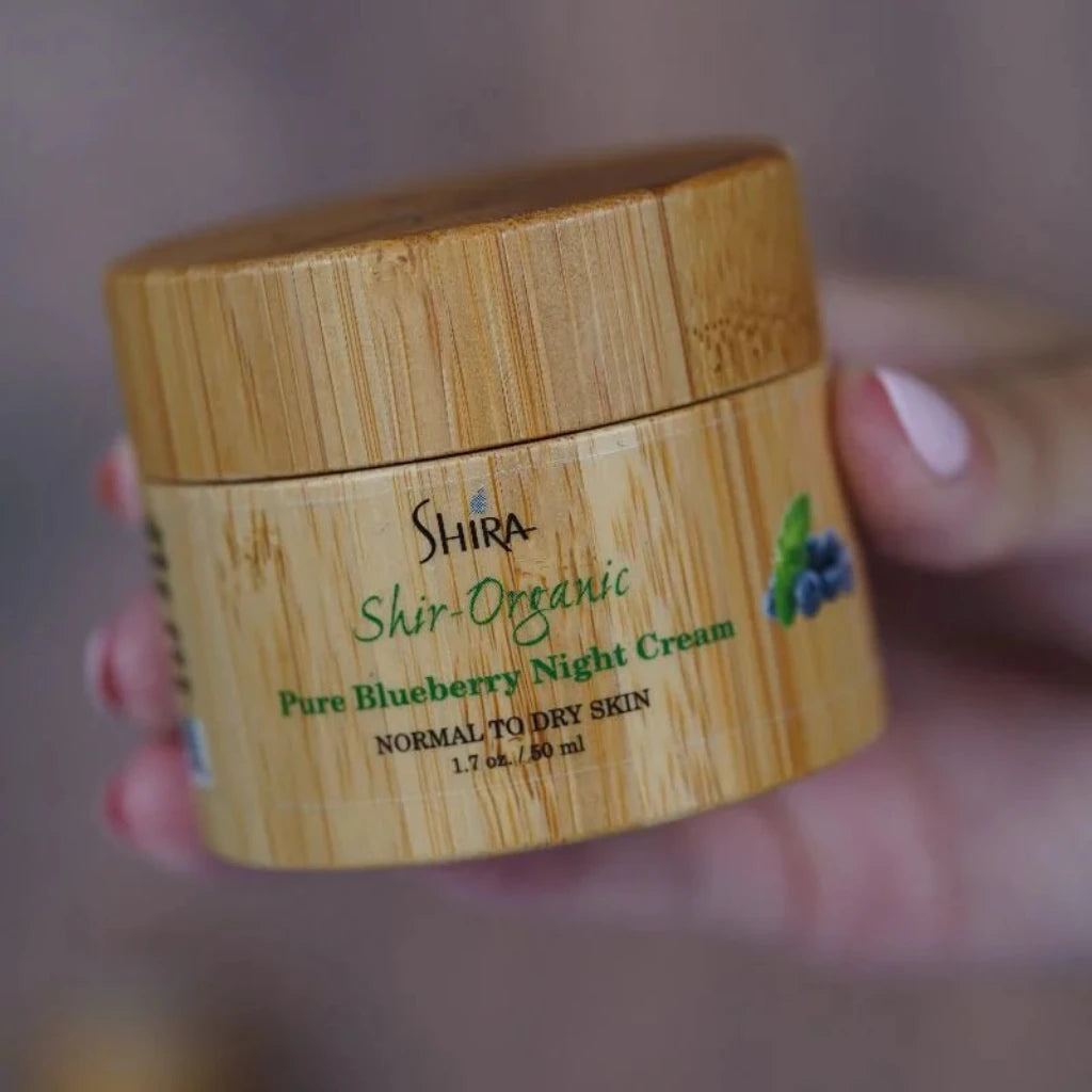 Shira Organic Pure Blueberry Night Cream jar held by a hand with a blurred background